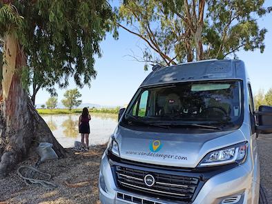 furgoneta de alquiler de Van de Camper aparcada bajo un árbol con un lago en el fondo