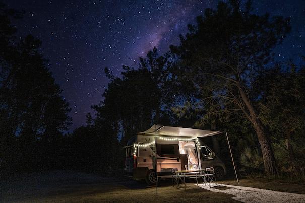 Camper de alquiler de VandeCamper aparcada de noche con luces y toldo bajo las estrellas